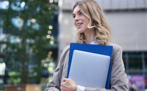 portrait-young-corporate-woman-office-manager-walking-street-with-laptop-work-folder-smili